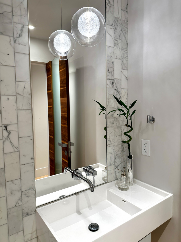 Bild på ett funkis vit vitt toalett, med luckor med glaspanel, vita skåp, marmorkakel, vita väggar, ljust trägolv och ett väggmonterat handfat
