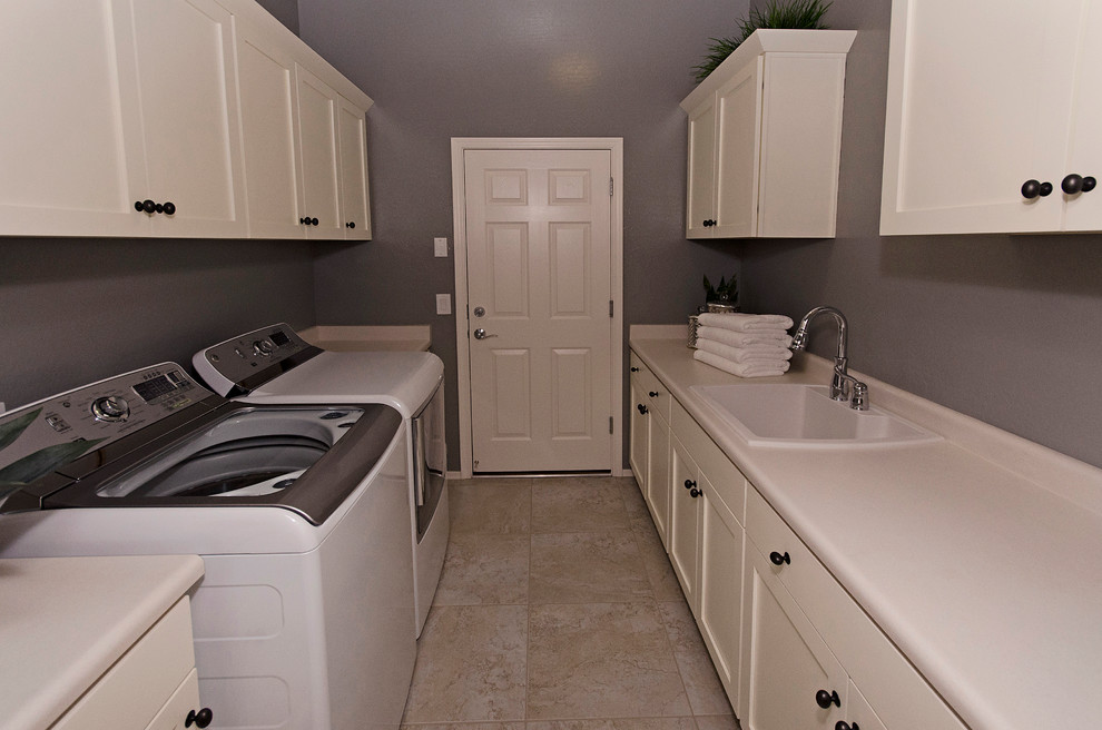 Photo of a mid-sized traditional galley utility room in Phoenix with a drop-in sink, recessed-panel cabinets, white cabinets, laminate benchtops, grey walls, porcelain floors and a side-by-side washer and dryer.