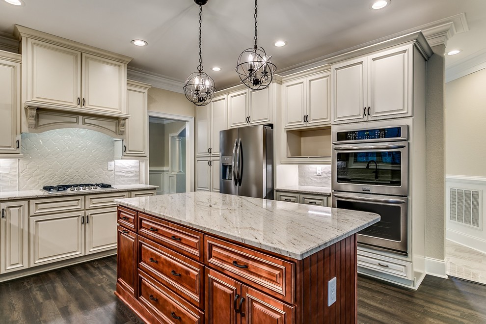 Photo of a large traditional eat-in kitchen in Other with a farmhouse sink, raised-panel cabinets, granite benchtops, beige splashback, subway tile splashback, stainless steel appliances, vinyl floors, with island, brown floor and beige benchtop.