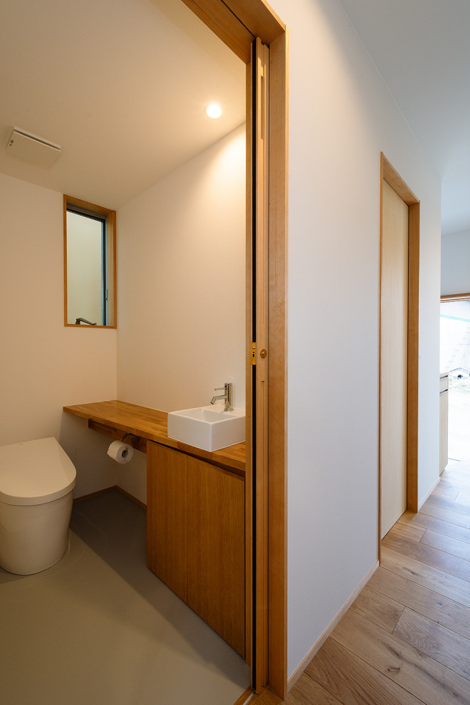 Inspiration för ett mellanstort minimalistiskt beige beige toalett, med släta luckor, skåp i mellenmörkt trä, en toalettstol med hel cisternkåpa, vita väggar, vinylgolv, ett fristående handfat, träbänkskiva och grått golv
