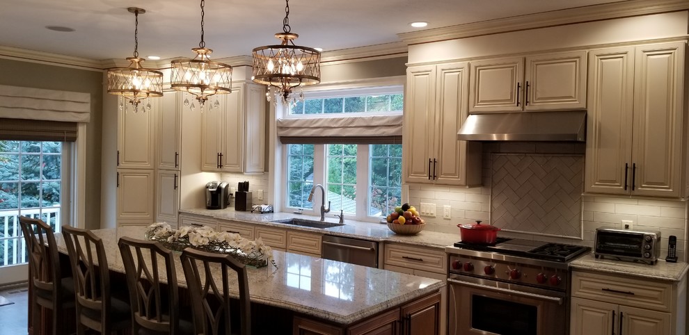 This is an example of a large traditional galley kitchen in Boston with an undermount sink, raised-panel cabinets, brown cabinets, granite benchtops, beige splashback, stainless steel appliances, dark hardwood floors, with island, brown floor, multi-coloured benchtop and porcelain splashback.
