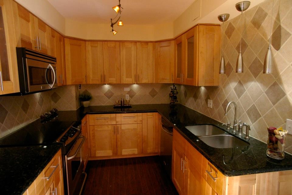 Small elegant u-shaped dark wood floor enclosed kitchen photo with a double-bowl sink, shaker cabinets, light wood cabinets, granite countertops, gray backsplash, ceramic backsplash, stainless steel appliances and no island