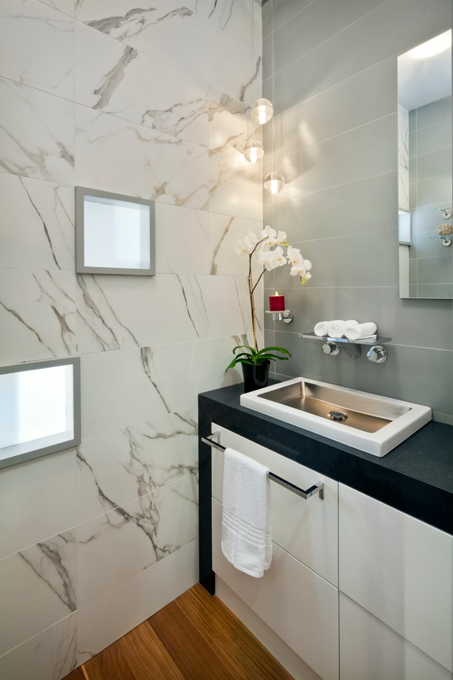 This is an example of a mid-sized contemporary powder room in San Francisco with a vessel sink, flat-panel cabinets, engineered quartz benchtops, gray tile, white tile, porcelain tile, multi-coloured walls, medium hardwood floors and white cabinets.