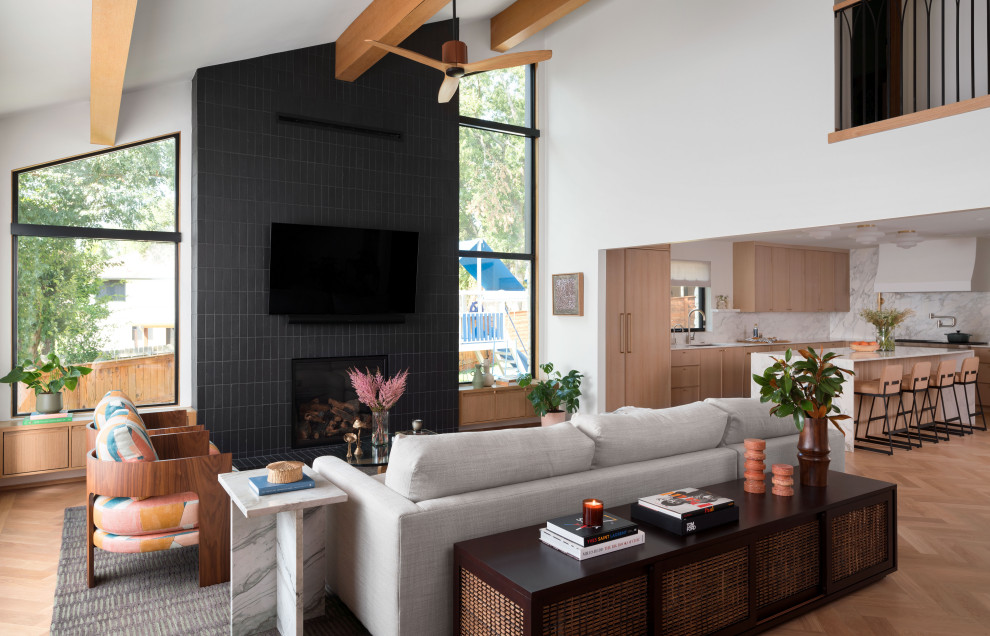 Источник вдохновения для домашнего уюта: открытая гостиная комната в стиле неоклассика (современная классика) с светлым паркетным полом, стандартным камином, фасадом камина из плитки, телевизором на стене и балками на потолке