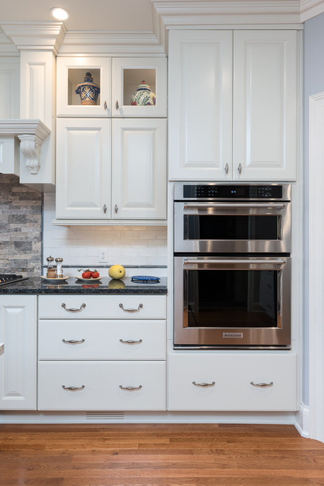 Open concept kitchen - large transitional single-wall light wood floor and brown floor open concept kitchen idea with a farmhouse sink, raised-panel cabinets, white cabinets, quartz countertops, white backsplash, ceramic backsplash, stainless steel appliances, an island and white countertops