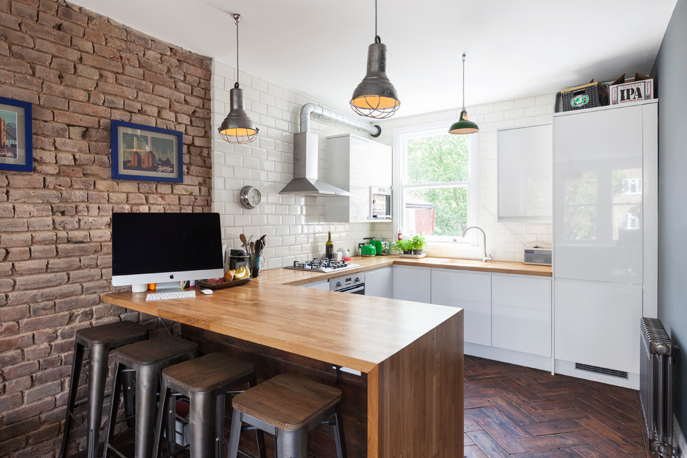 Design ideas for a contemporary u-shaped open plan kitchen in London with flat-panel cabinets, white cabinets, wood benchtops, subway tile splashback, stainless steel appliances, dark hardwood floors and a peninsula.