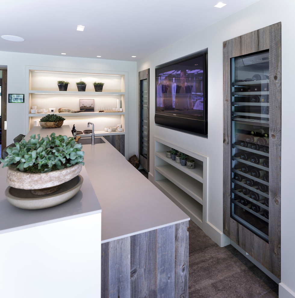This is an example of a mid-sized contemporary galley wet bar in Cheshire with a drop-in sink, flat-panel cabinets, medium wood cabinets, concrete benchtops, white splashback, ceramic splashback, ceramic floors and grey floor.