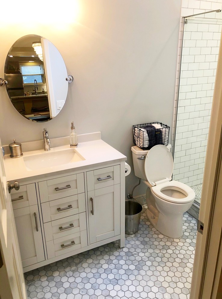 This is an example of a mid-sized traditional 3/4 bathroom in Detroit with shaker cabinets, white cabinets, an alcove shower, a two-piece toilet, white tile, subway tile, grey walls, ceramic floors, an undermount sink, granite benchtops, grey floor, a hinged shower door, white benchtops and a freestanding vanity.