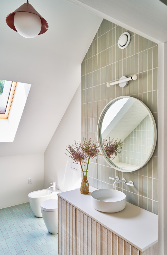 This is an example of a scandinavian cloakroom in New York with light wood cabinets, a wall mounted toilet, green tiles, white walls, ceramic flooring, a vessel sink, engineered stone worktops, turquoise floors, white worktops and a vaulted ceiling.