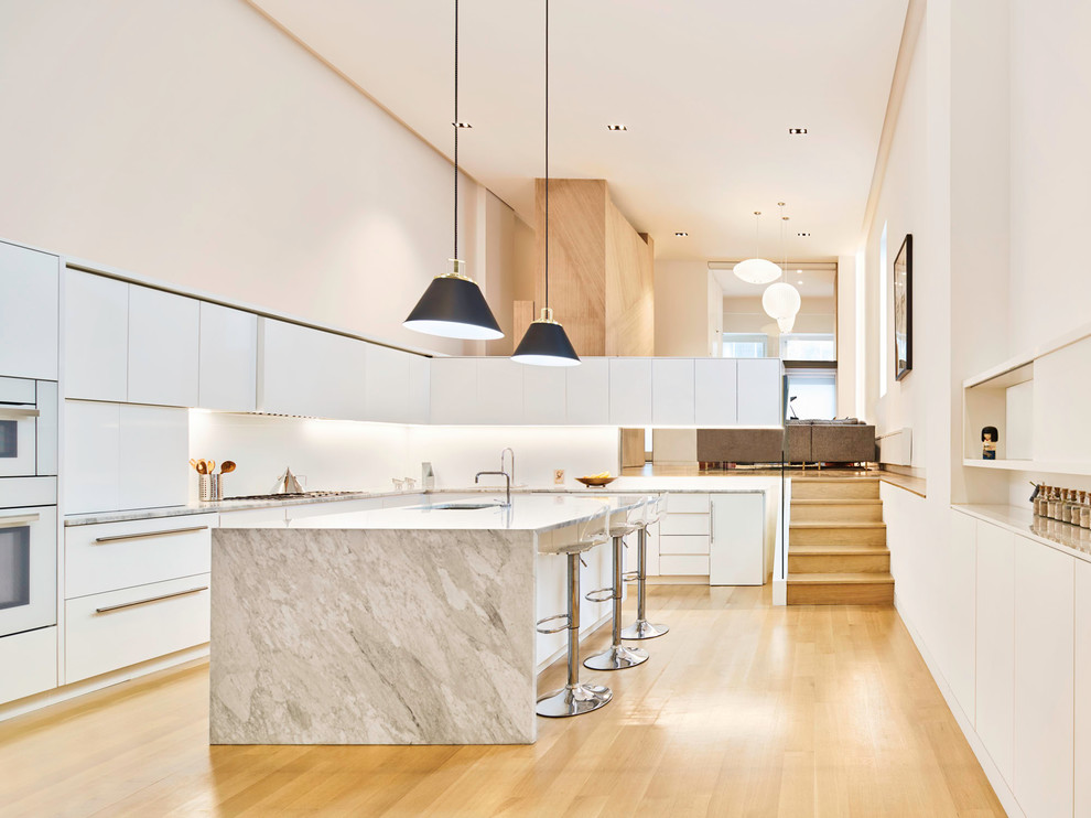 Design ideas for a modern l-shaped kitchen in New York with flat-panel cabinets, white cabinets, white splashback, white appliances, light hardwood floors, with island, beige floor and white benchtop.
