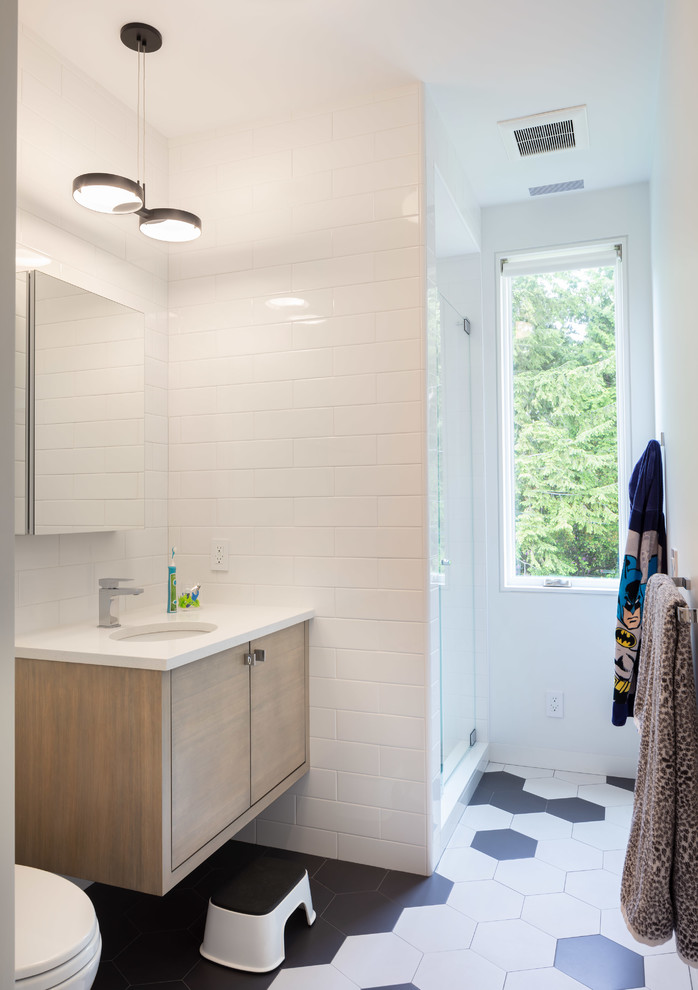 Design ideas for a mid-sized contemporary kids bathroom in Providence with flat-panel cabinets, medium wood cabinets, white tile, porcelain tile, white walls, porcelain floors, an undermount sink, engineered quartz benchtops, multi-coloured floor, a hinged shower door and white benchtops.