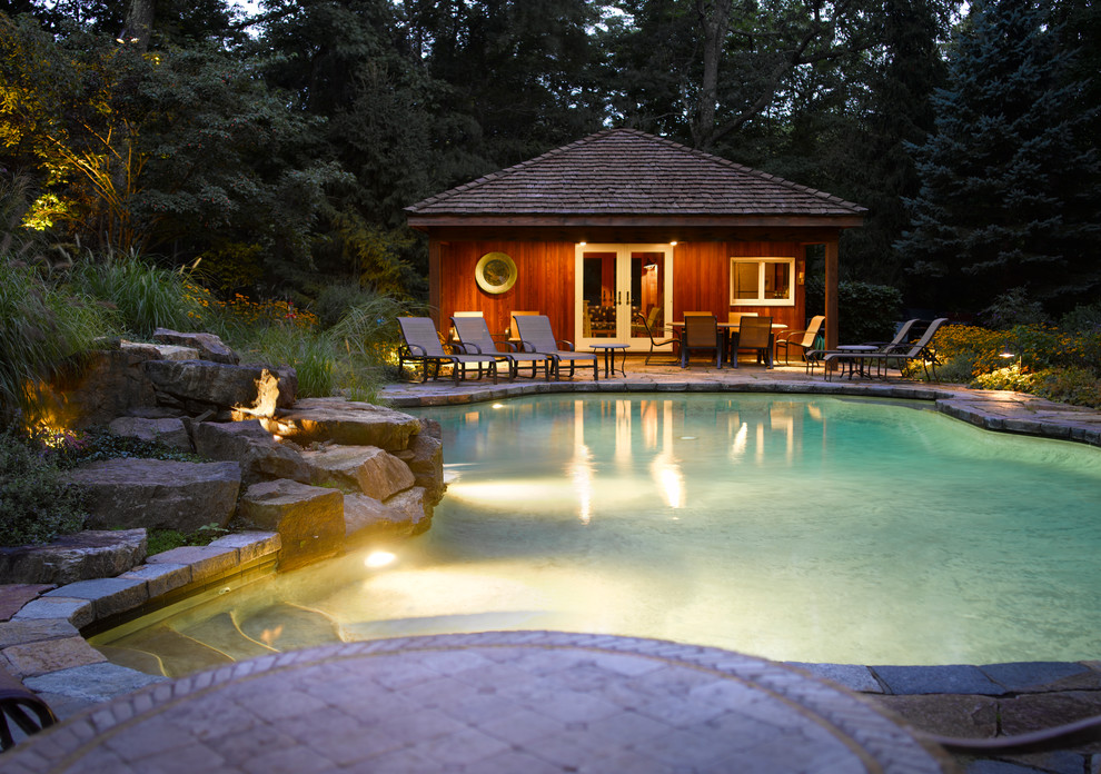 Design ideas for a tropical backyard custom-shaped pool in New York with a pool house and natural stone pavers.
