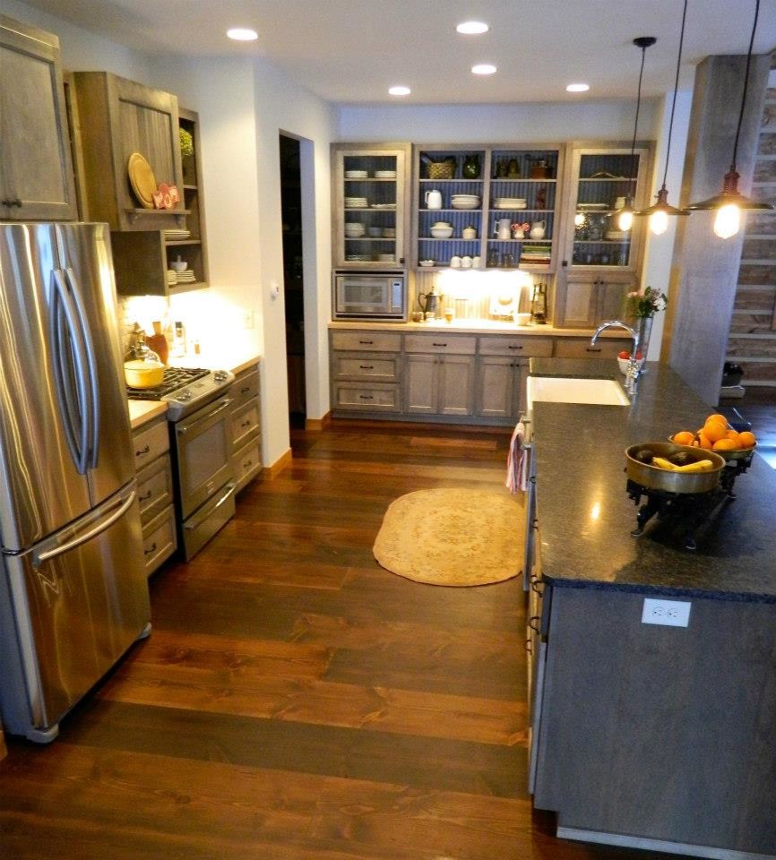 This is an example of a mid-sized country galley eat-in kitchen in Minneapolis with a farmhouse sink, glass-front cabinets, medium wood cabinets, granite benchtops, brown splashback, stone tile splashback, stainless steel appliances, dark hardwood floors and with island.
