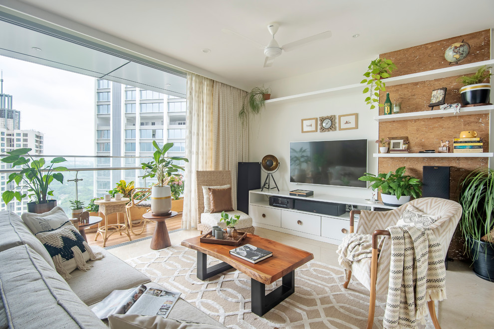 This is an example of a tropical living room in Mumbai with white walls, a wall-mounted tv and beige floor.
