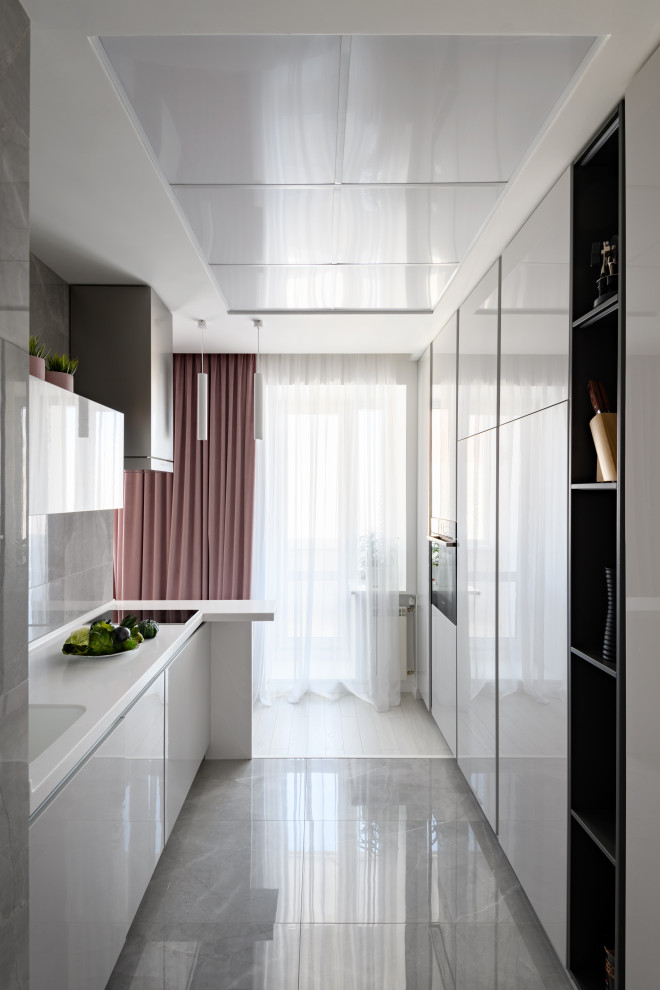 Inspiration for a mid-sized contemporary galley kitchen in Novosibirsk with an undermount sink, flat-panel cabinets, white cabinets, grey splashback, glass sheet splashback, panelled appliances, no island, grey floor and white benchtop.