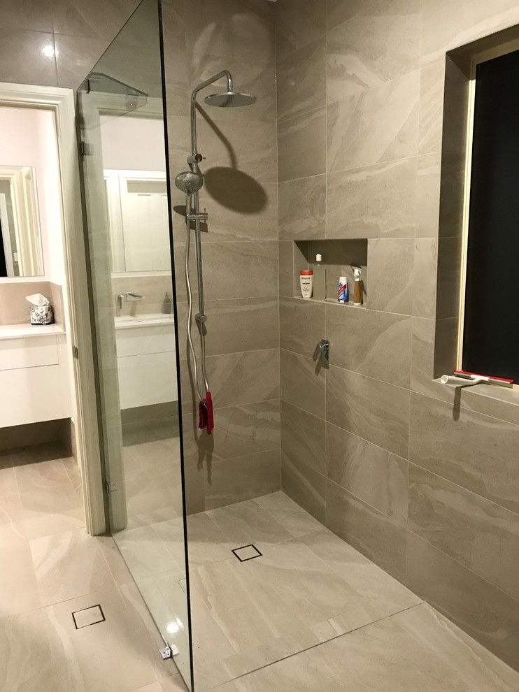This is an example of a medium sized contemporary ensuite bathroom in Adelaide with flat-panel cabinets, white cabinets, an alcove shower, a two-piece toilet, beige tiles, ceramic tiles, white walls, ceramic flooring, a submerged sink, engineered stone worktops, beige floors, an open shower and white worktops.