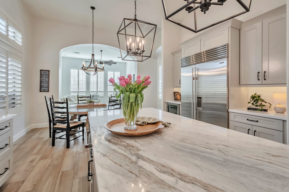 Example of a large transitional u-shaped porcelain tile, brown floor and exposed beam kitchen design in Phoenix with a farmhouse sink, shaker cabinets, gray cabinets, quartzite countertops, white backsplash, porcelain backsplash, stainless steel appliances, an island and white countertops