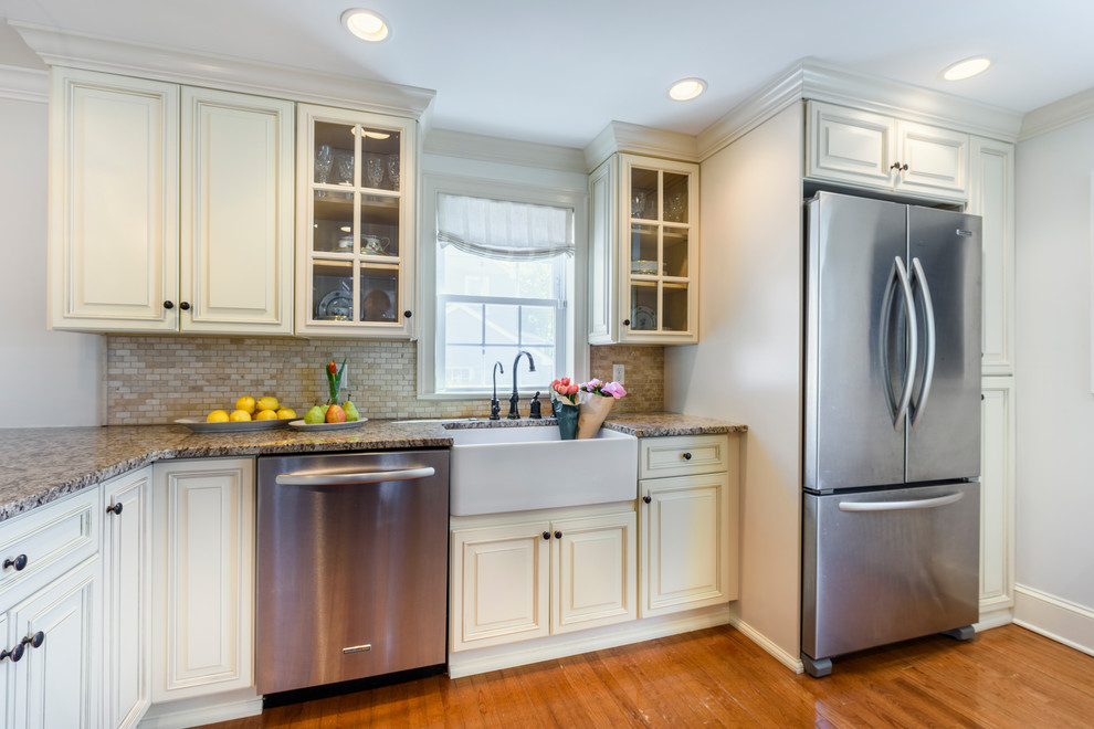 Mid-sized transitional l-shaped medium tone wood floor and brown floor enclosed kitchen photo in Philadelphia with a farmhouse sink, raised-panel cabinets, beige cabinets, granite countertops, beige backsplash, mosaic tile backsplash, stainless steel appliances and an island