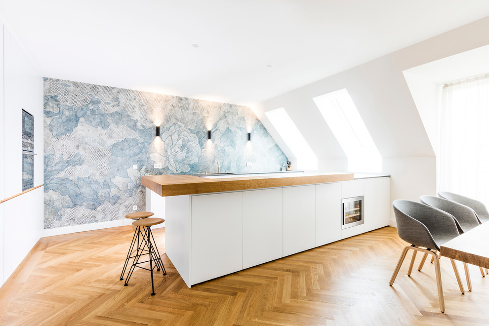 Design ideas for a large scandinavian l-shaped eat-in kitchen in Munich with flat-panel cabinets, white cabinets, wood benchtops, light hardwood floors, with island, beige floor, beige benchtop, multi-coloured splashback and stainless steel appliances.