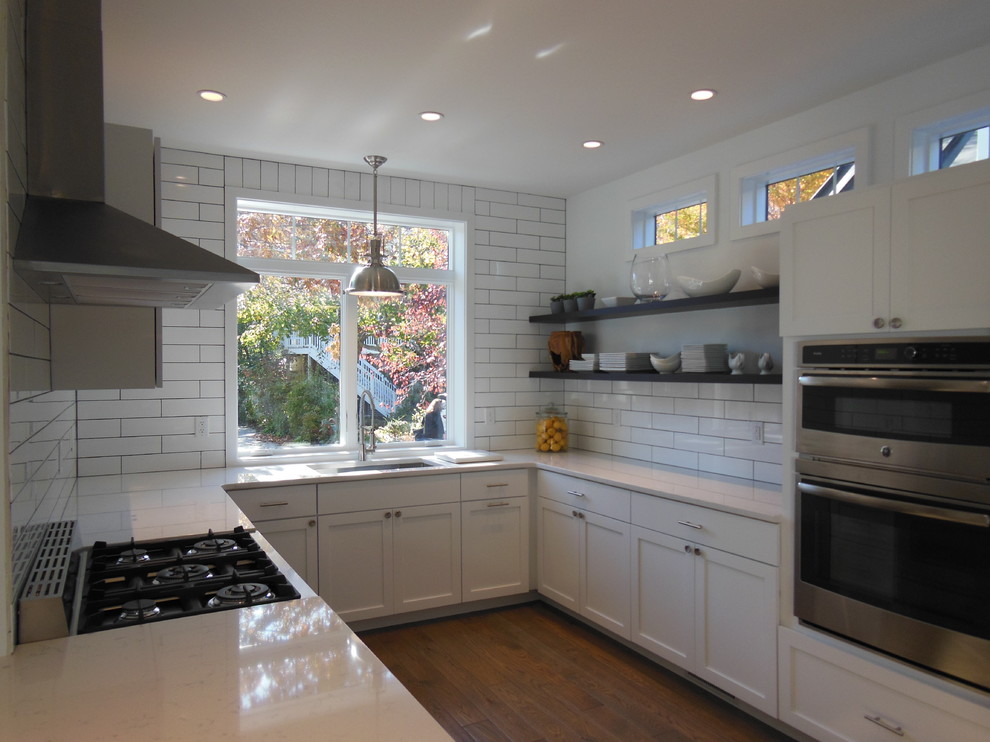 This is an example of a large country u-shaped open plan kitchen in Philadelphia with a single-bowl sink, flat-panel cabinets, white cabinets, granite benchtops, white splashback, ceramic splashback, stainless steel appliances, dark hardwood floors and with island.