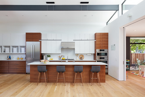 Modern open-plan kitchen with white and wood kitchen cabinet fronts, large island, and four bar stools on light oak flooring.