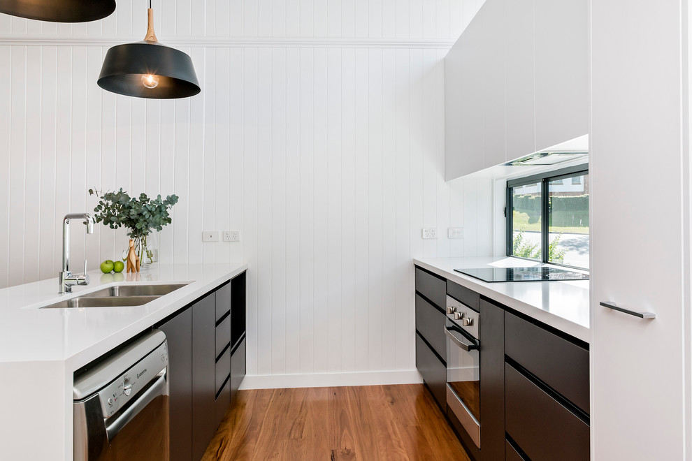 Photo of a mid-sized modern galley open plan kitchen in Brisbane with an undermount sink, flat-panel cabinets, black cabinets, quartz benchtops, multi-coloured splashback, glass sheet splashback, stainless steel appliances, medium hardwood floors and with island.