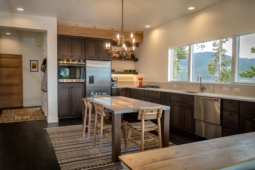 This is an example of a mid-sized country l-shaped open plan kitchen in Denver with an undermount sink, shaker cabinets, dark wood cabinets, quartz benchtops, white splashback, stainless steel appliances, laminate floors, with island, brown floor and white benchtop.