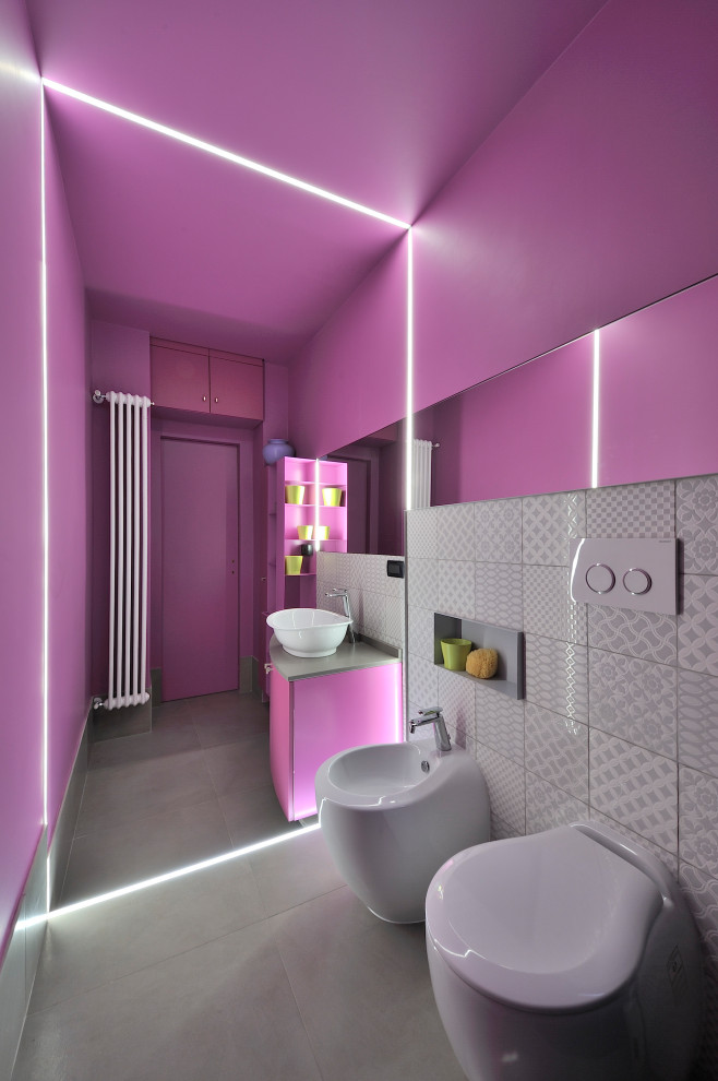 Modelo de aseo flotante actual pequeño con sanitario de dos piezas, paredes rosas, lavabo sobreencimera, suelo gris y encimeras grises