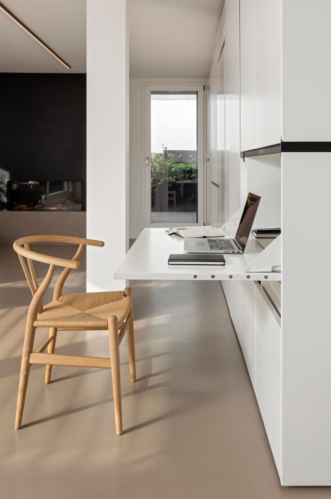 Modern inredning av ett mellanstort hemmastudio, med vita väggar, betonggolv, en bred öppen spis, en spiselkrans i metall, ett inbyggt skrivbord och grått golv