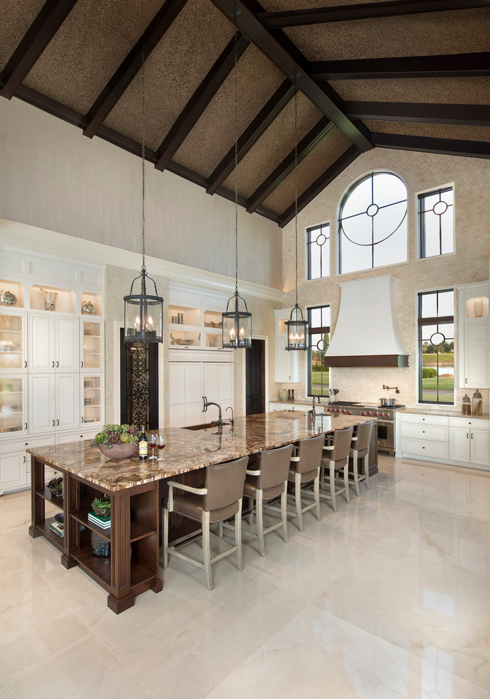 Inspiration for an expansive mediterranean eat-in kitchen in Miami with a farmhouse sink, white cabinets, granite benchtops, limestone splashback, panelled appliances, marble floors, with island, beige splashback, beige floor and glass-front cabinets.