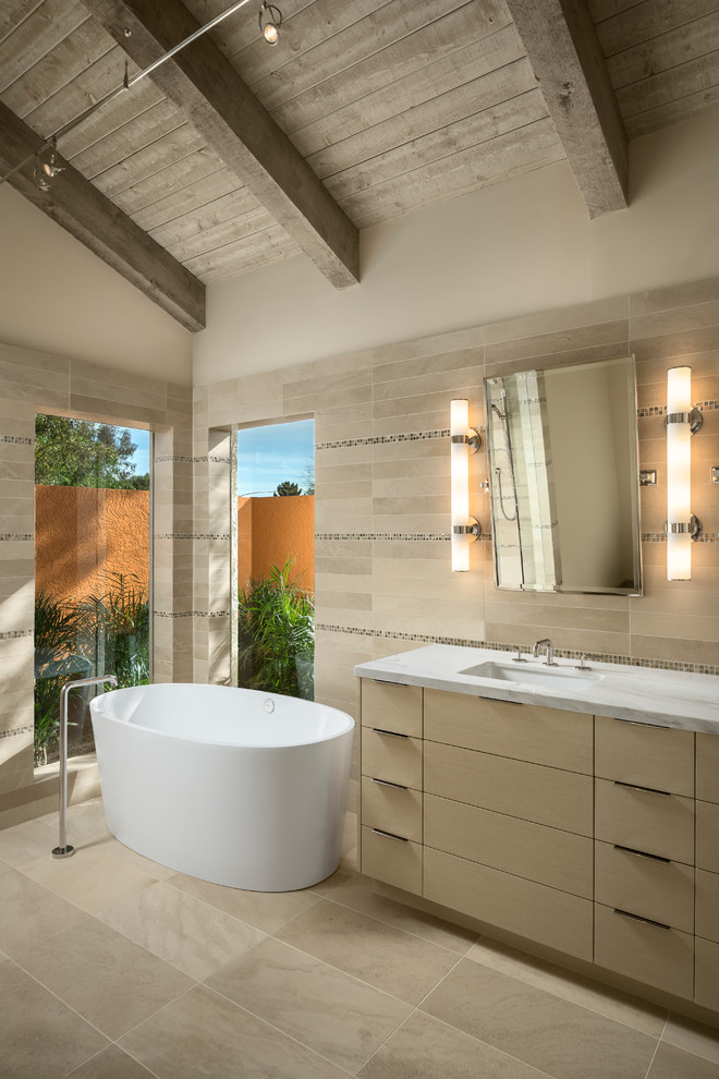 Photo of a large contemporary master bathroom in Phoenix with beige cabinets, a freestanding tub, beige tile, ceramic tile, beige walls, limestone floors, marble benchtops, beige floor, flat-panel cabinets and an undermount sink.