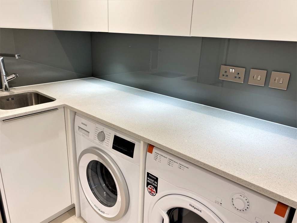 Small l-shaped utility room in London with flat-panel cabinets, white cabinets, quartzite benchtops, brown splashback, glass sheet splashback, white walls, a side-by-side washer and dryer and white benchtop.