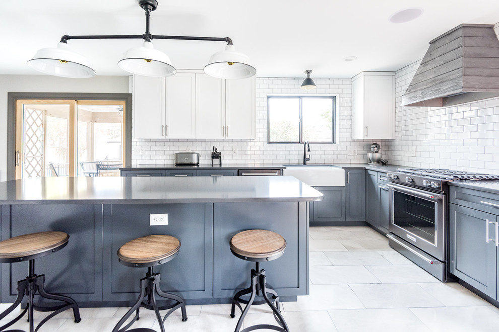 This is an example of a large country l-shaped kitchen in Wilmington with a farmhouse sink, shaker cabinets, blue cabinets, white splashback, subway tile splashback, with island, quartz benchtops, black appliances, marble floors, grey floor and black benchtop.