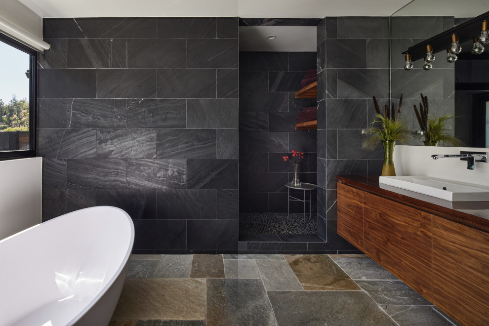 Inspiration for a large midcentury master wet room bathroom in Los Angeles with furniture-like cabinets, brown cabinets, a freestanding tub, a one-piece toilet, black tile, slate, white walls, slate floors, a vessel sink, wood benchtops, multi-coloured floor, an open shower and brown benchtops.