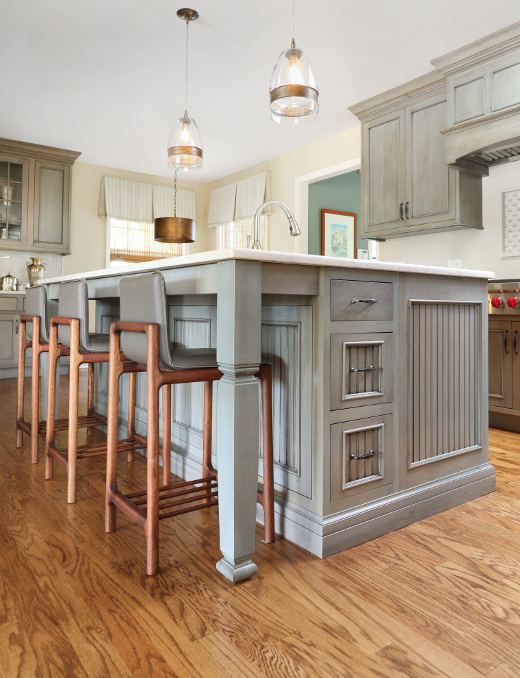 This is an example of a large traditional l-shaped eat-in kitchen in Chicago with flat-panel cabinets, green cabinets, quartz benchtops, white splashback, ceramic splashback, medium hardwood floors, with island, brown floor and white benchtop.