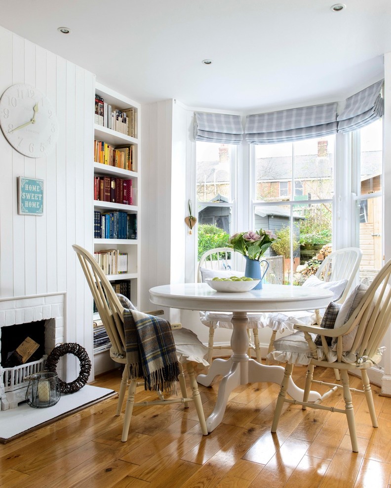 This is an example of a small beach style dining room in Kent with white walls, medium hardwood floors, a standard fireplace and a brick fireplace surround.