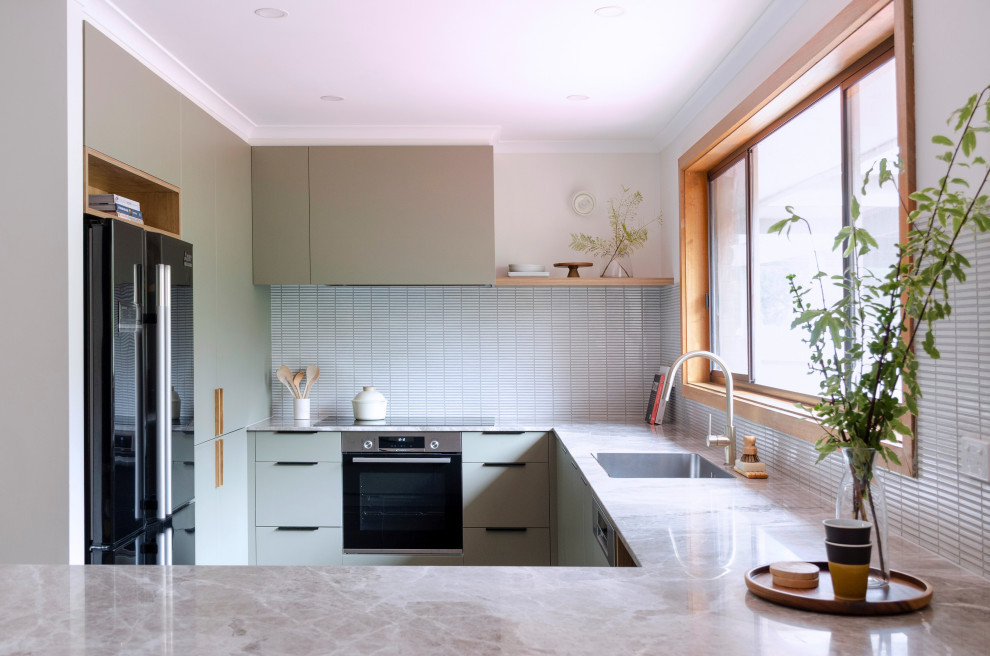 Design ideas for a mid-sized midcentury u-shaped kitchen pantry in Melbourne with a single-bowl sink, flat-panel cabinets, green cabinets, limestone benchtops, white splashback, mosaic tile splashback, black appliances, slate floors, a peninsula, brown floor and beige benchtop.