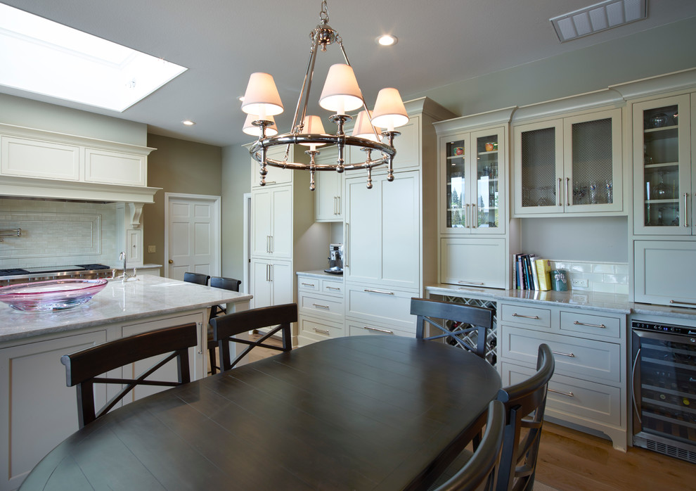 Inspiration for a mid-sized transitional l-shaped medium tone wood floor eat-in kitchen remodel with a farmhouse sink, recessed-panel cabinets, white cabinets, marble countertops, white backsplash, subway tile backsplash, stainless steel appliances and an island