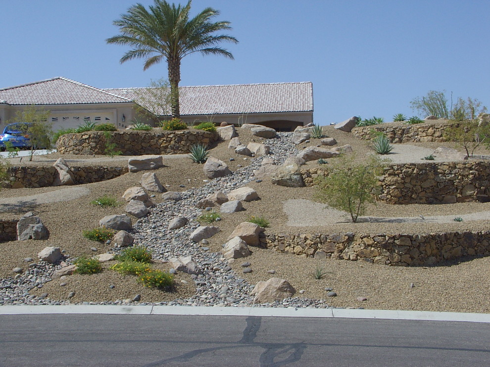 This is an example of a small and desert look front yard full sun xeriscape for summer in Other with brick pavers and a stone fence.