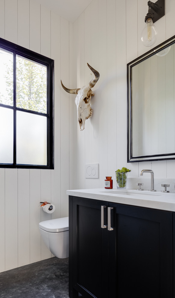 This is an example of a transitional powder room in San Francisco with shaker cabinets, black cabinets, a wall-mount toilet, white walls, an undermount sink and grey floor.