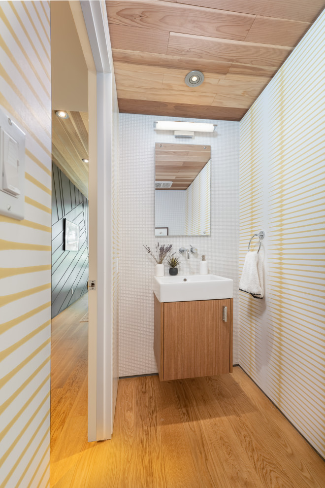 Small contemporary powder room in Los Angeles with medium wood cabinets, a one-piece toilet, white tile, pebble tile, an integrated sink, white benchtops, a built-in vanity, wood and wallpaper.