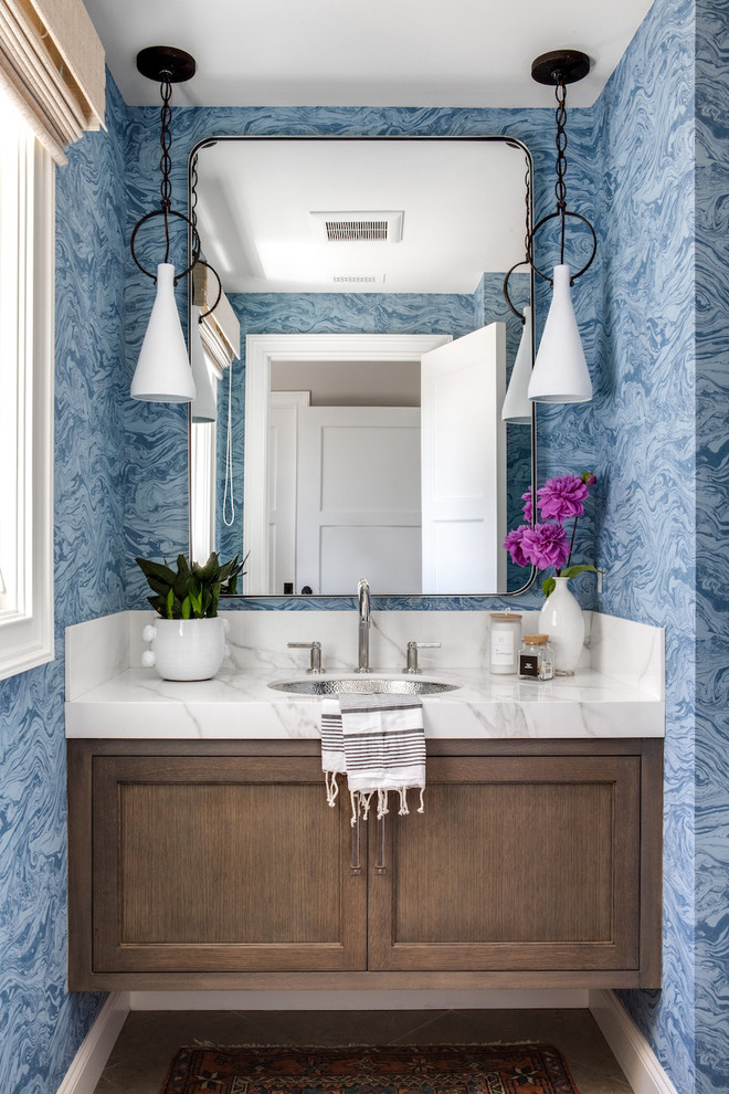Inspiration for a transitional powder room in Orange County with recessed-panel cabinets, dark wood cabinets, blue walls, an undermount sink, brown floor and white benchtops.