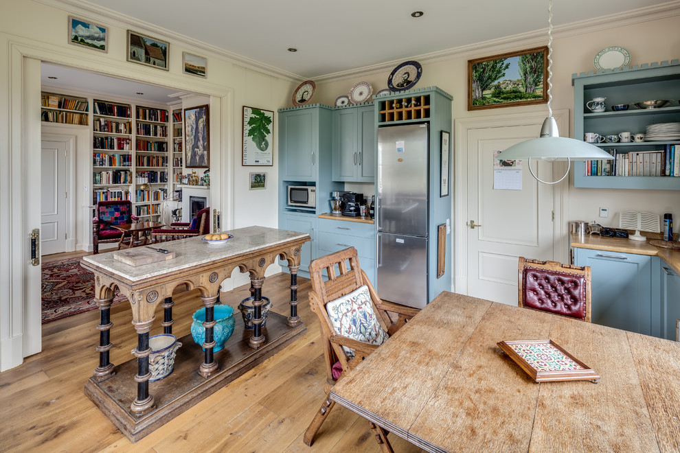 Photo of a traditional eat-in kitchen in Wiltshire with shaker cabinets, blue cabinets, wood benchtops, stainless steel appliances, light hardwood floors and with island.