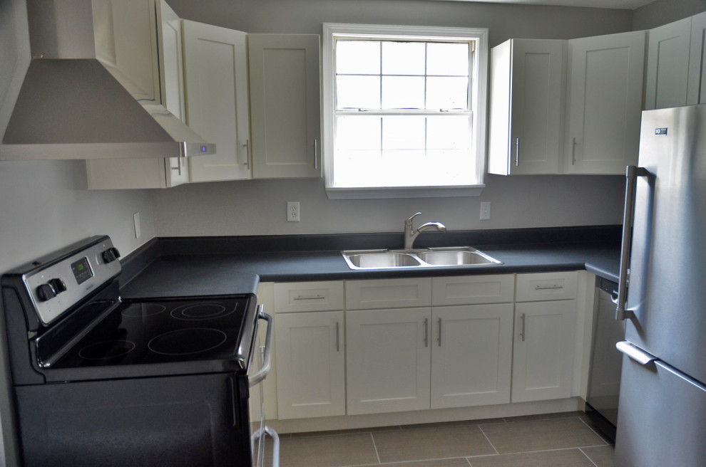 Inspiration for a mid-sized u-shaped porcelain tile and beige floor eat-in kitchen remodel with a drop-in sink, shaker cabinets, white cabinets, laminate countertops, stainless steel appliances, no island and black countertops