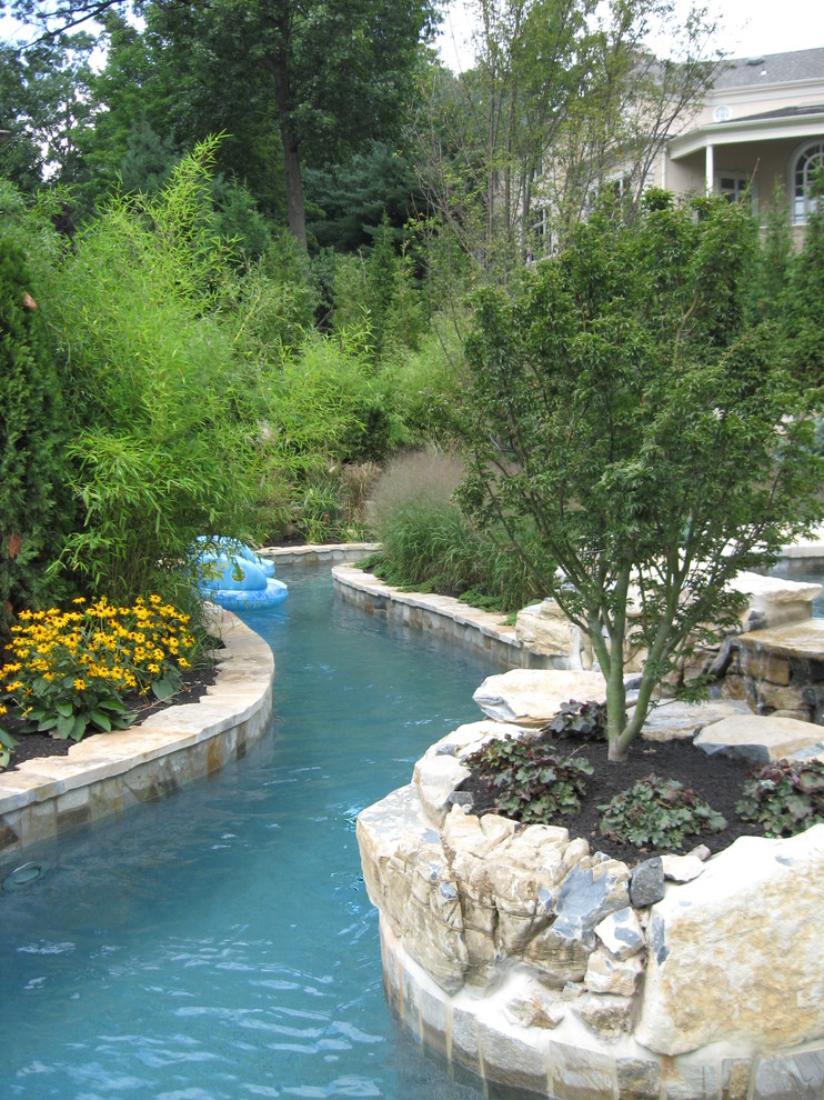 This is an example of an expansive transitional backyard custom-shaped natural pool in New York with a water feature and natural stone pavers.