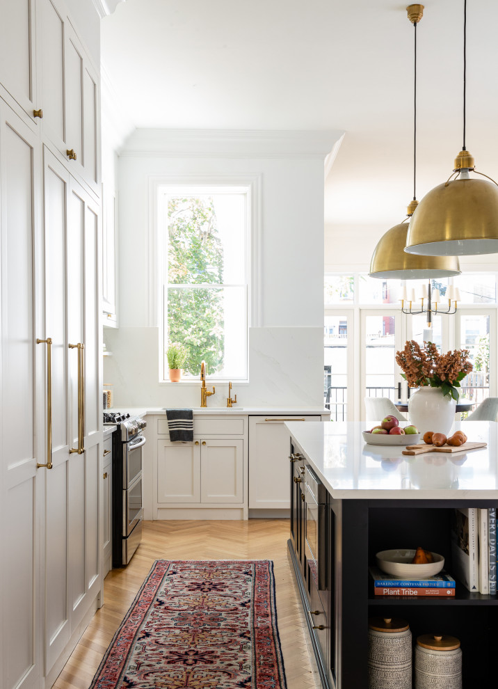 Klassisk inredning av ett mellanstort vit vitt kök, med en undermonterad diskho, luckor med profilerade fronter, vita skåp, bänkskiva i kvarts, integrerade vitvaror, ljust trägolv och en köksö