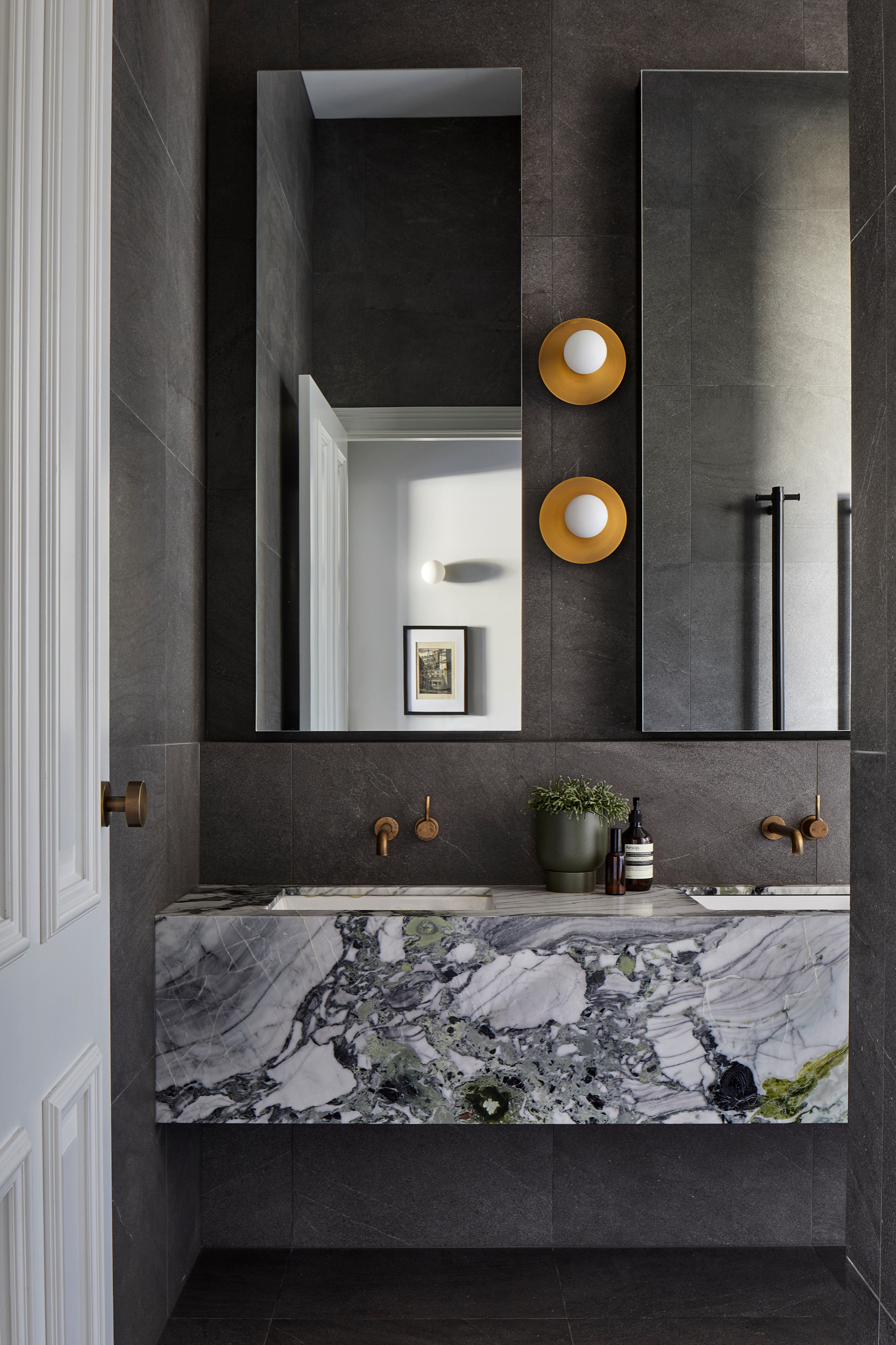 Renovated black bathroom with brass fixtures and marble tile clad