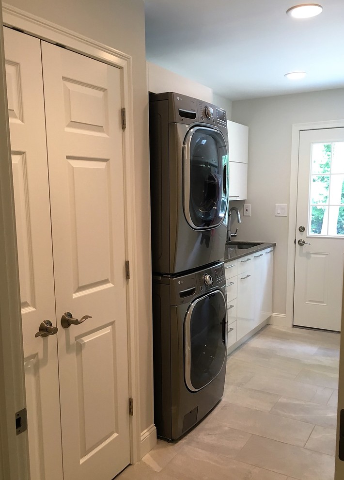 Inspiration for a small transitional single-wall dedicated laundry room in Philadelphia with an undermount sink, flat-panel cabinets, white cabinets, quartz benchtops, grey walls, light hardwood floors and a stacked washer and dryer.