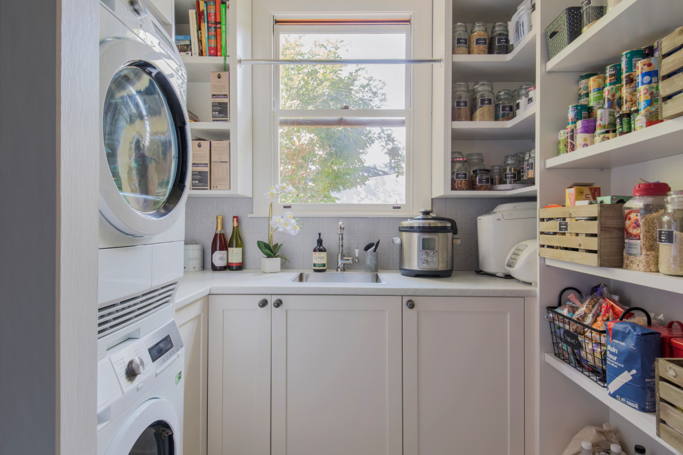 Small transitional u-shaped utility room in Sydney with a single-bowl sink, shaker cabinets, white cabinets, quartz benchtops, grey walls, ceramic floors, a stacked washer and dryer, brown floor and white benchtop.