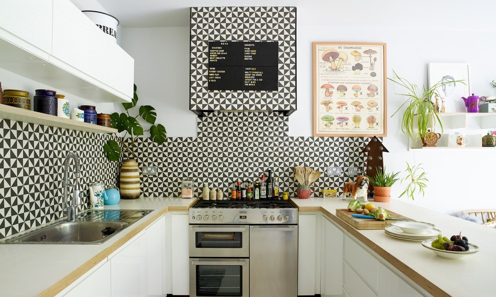 Mid-sized eclectic u-shaped eat-in kitchen in London with a double-bowl sink, flat-panel cabinets, white cabinets, wood benchtops, white splashback, cement tile splashback, stainless steel appliances, painted wood floors, a peninsula, white floor and white benchtop.